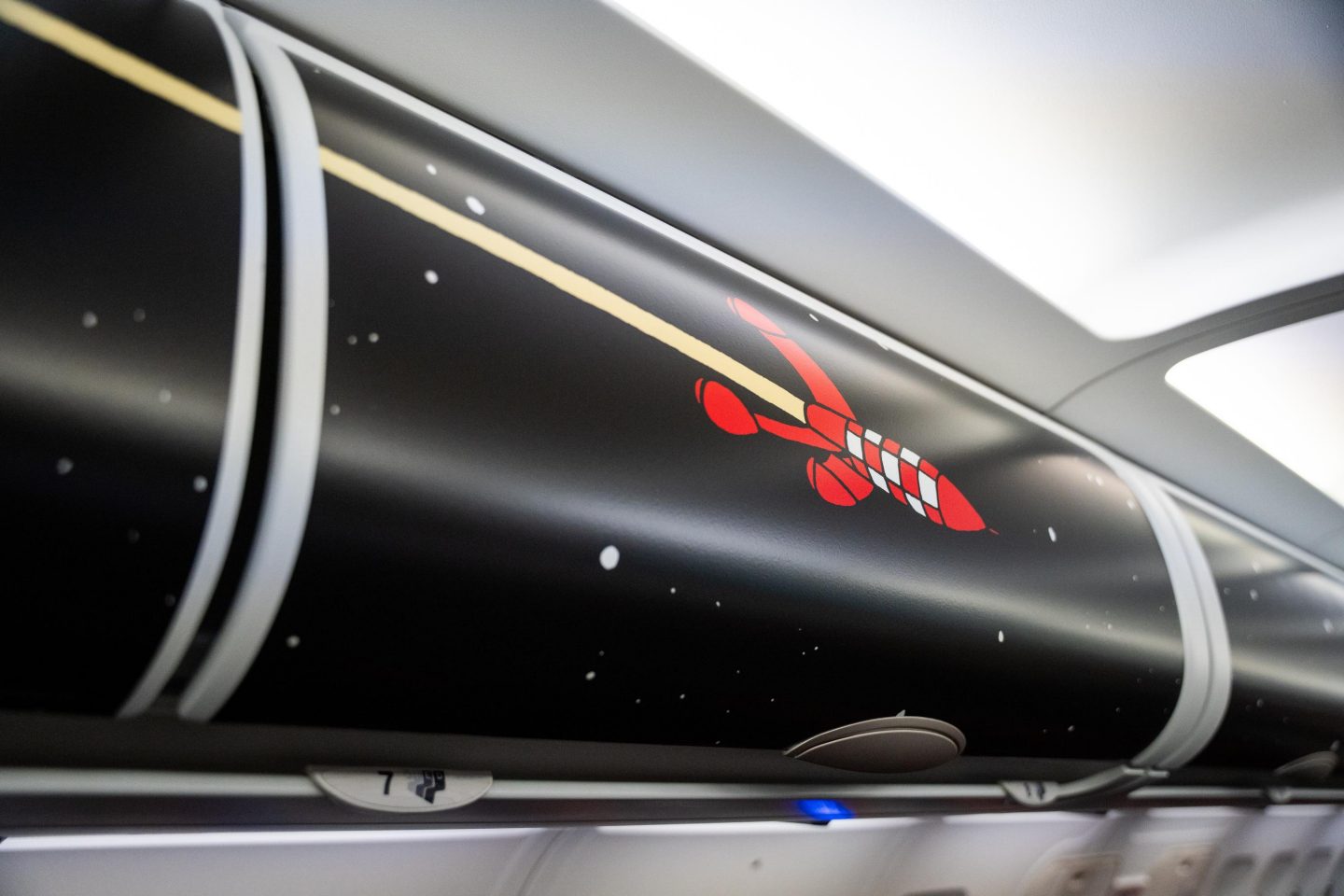 Airplane overhead bin displaying a red and white Tintin space rocket on a starry background.