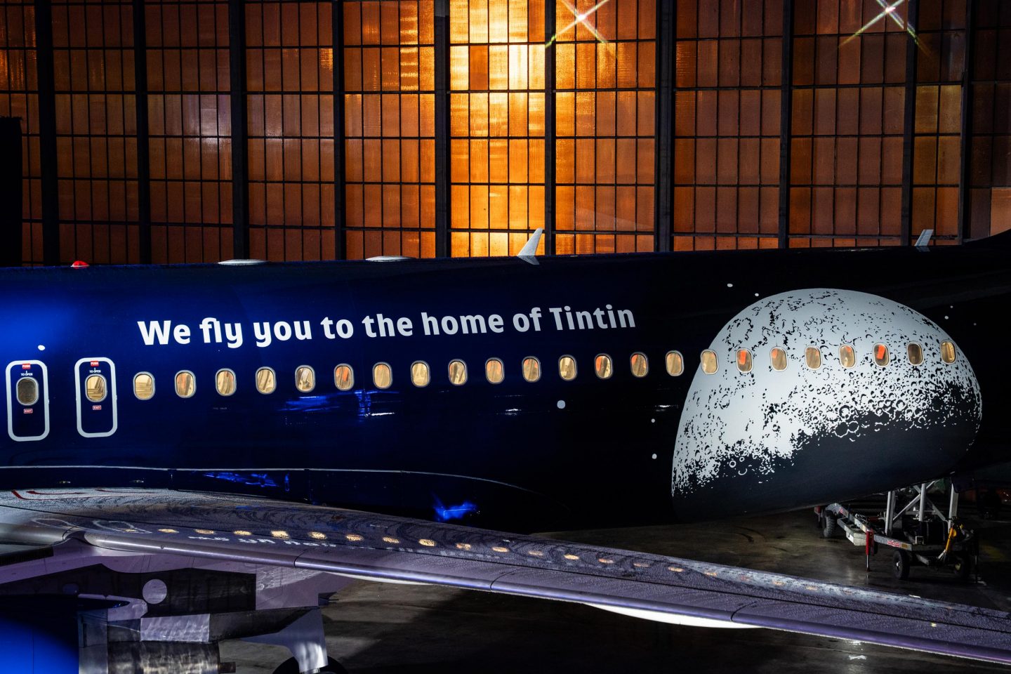 Airplane fuselage painted with a moon graphic and the text We fly you to the home of Tintin