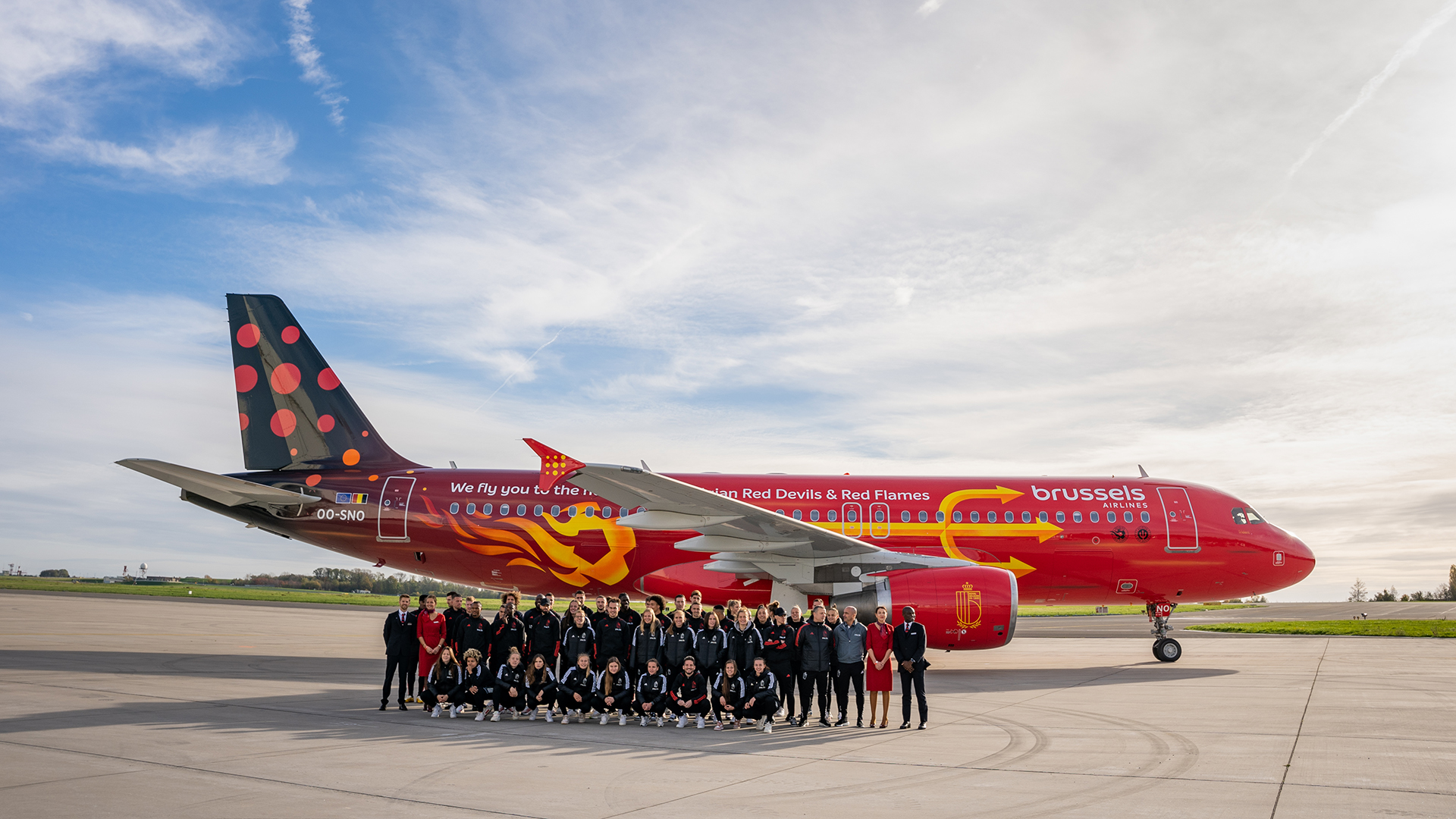 A large group posing in front of the red Brussels Airlines Trident airplane.