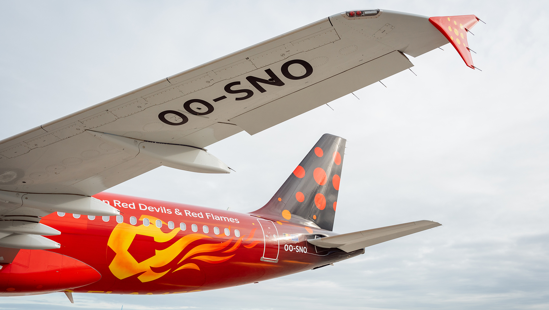Close-up of the tail and wing of the red Brussels Airlines Trident airplane, featuring a yellow flame design.