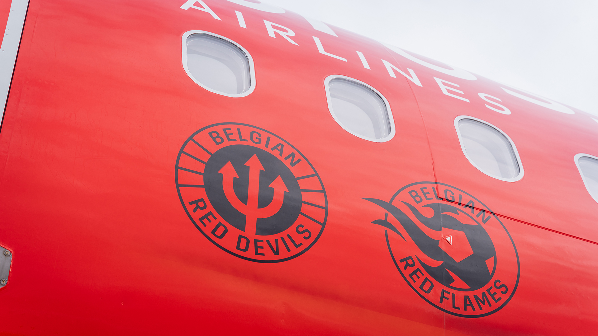 Red airplane fuselage displaying the circular Belgian Red Devils and Belgian Red Flames logos
