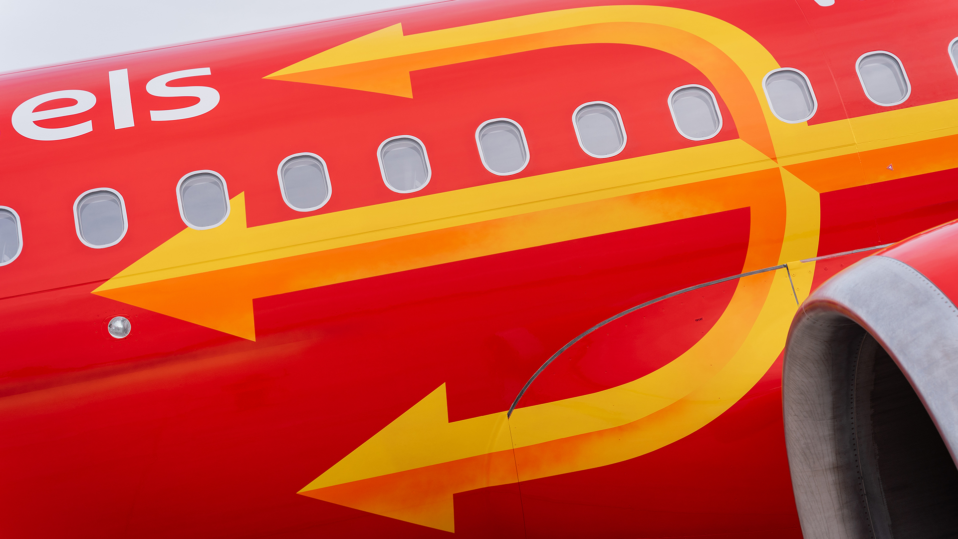 Red airplane fuselage with large yellow trident graphic winding around passenger windows
