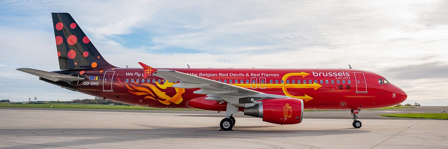 A red Brussels Airlines airplane with a yellow trident design parked on a tarmac.