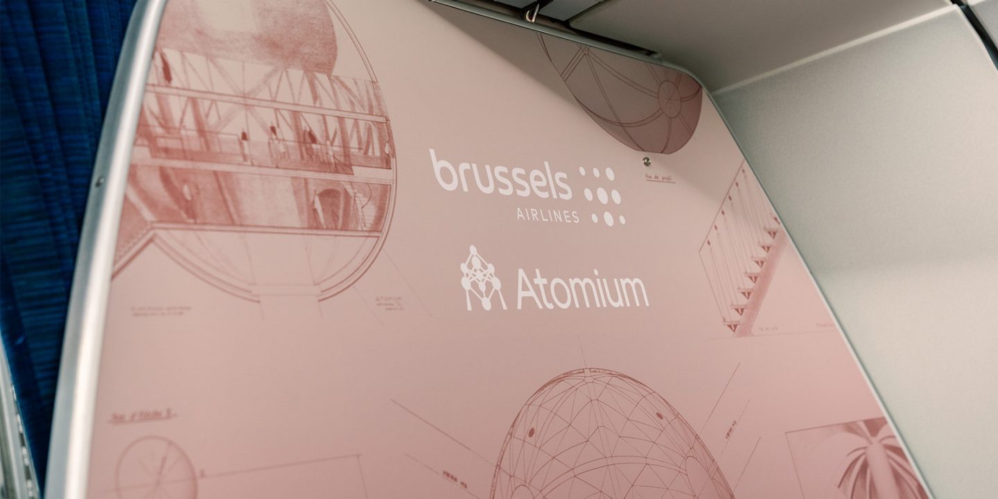 Airplane cabin bulkhead featuring pink Atomium sketches and branding.