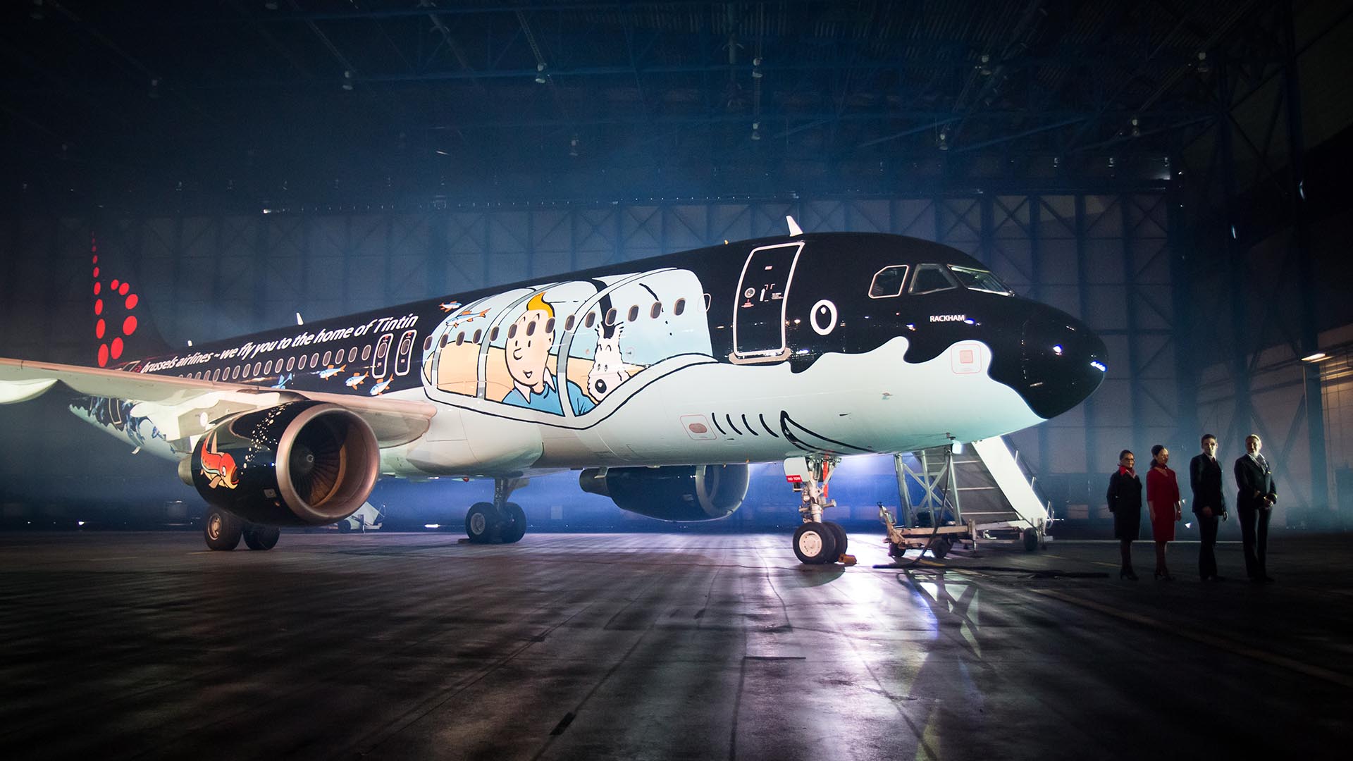 Brussels Airlines Rackham aircraft painted in a Tintin submarine livery, parked in a hangar with four crew members standing nearby.