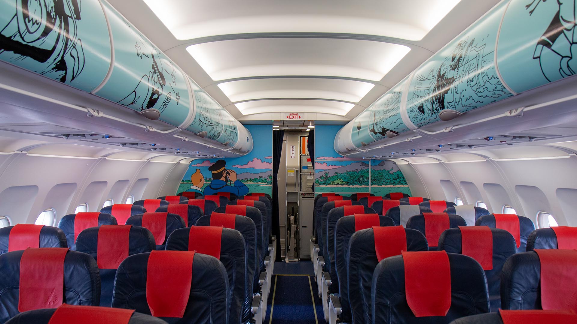 Interior of an aircraft cabin with blue and red seats, featuring Tintin comic strip murals on the overhead bins and rear wall.