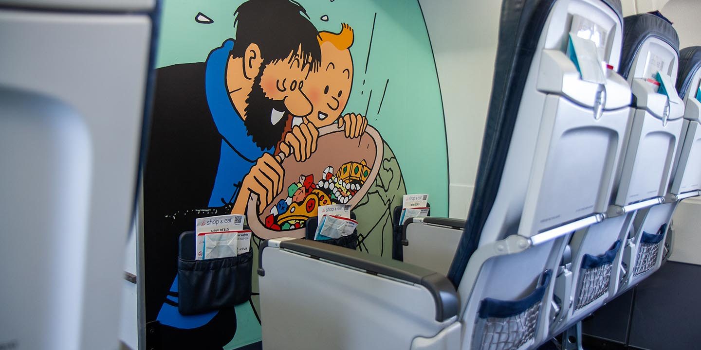 Interior of the Rackham aircraft cabin showing a wall mural of Captain Haddock and Tintin behind passenger seats.