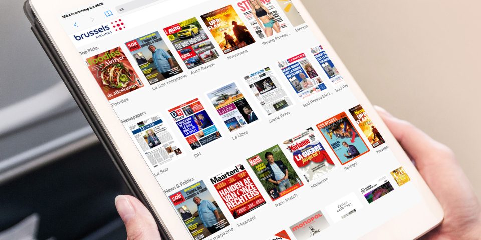 Hands holding a tablet displaying a selection of digital newspapers and magazines.